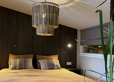 Modern hotel bedroom with dark accent wall, yellow bedding, crystal chandelier, and striped decorative pillows